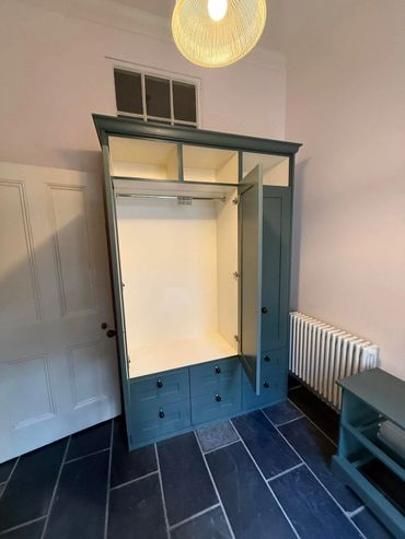 Open green wardrobe with multiple drawers and compartments in a room.