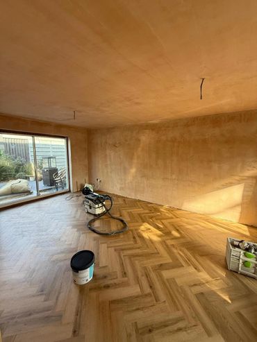 An empty room with freshly plastered walls and wooden herringbone flooring under renovation.