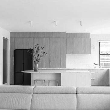 Modern minimalist kitchen with wooden cabinets and a sofa in foreground.