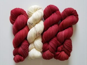 Four skeins of Emir merino cashmere yarn in the colorways Incendio (red) and Winterbark (cream).