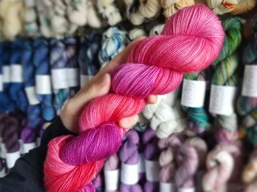 A hand holding a pink and purple skein on gold glitter base, Leila.