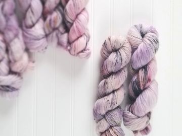 Multiple skeins of the colorway Fake Love, inspired by the BTS song of the same name, with a focus on a tweed skein and a mohair/wool skein.