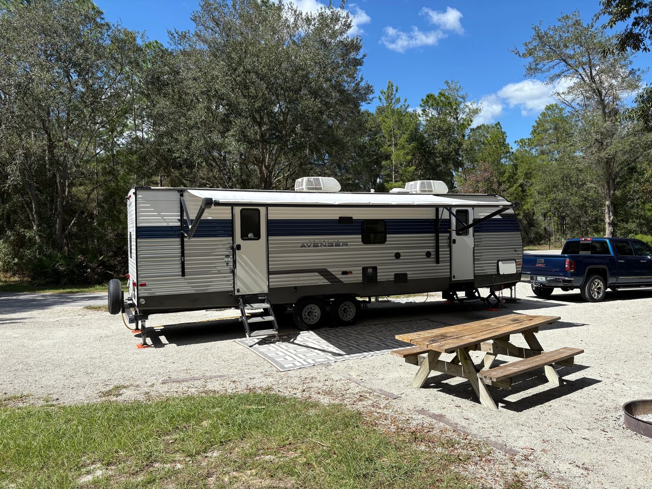 Travel trailer parked at a campsite with picnic table and truck nearby.