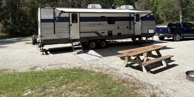 A parked travel trailer with a picnic table nearby in a wooded area.