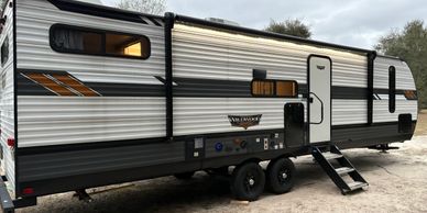 Modern travel trailer parked outdoors with stairs extended.