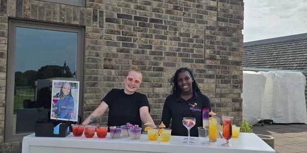 Two women standing behind a Vibez Mocktails bar with colorful drinks.