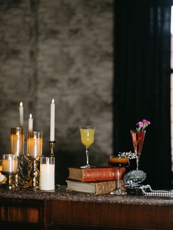 Elegant candles, vintage books, and cocktails on a polished wooden surface.