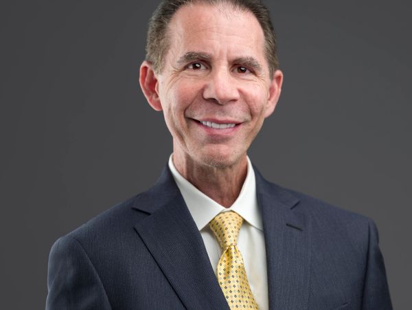 Professional man in a suit smiling against a gray background.