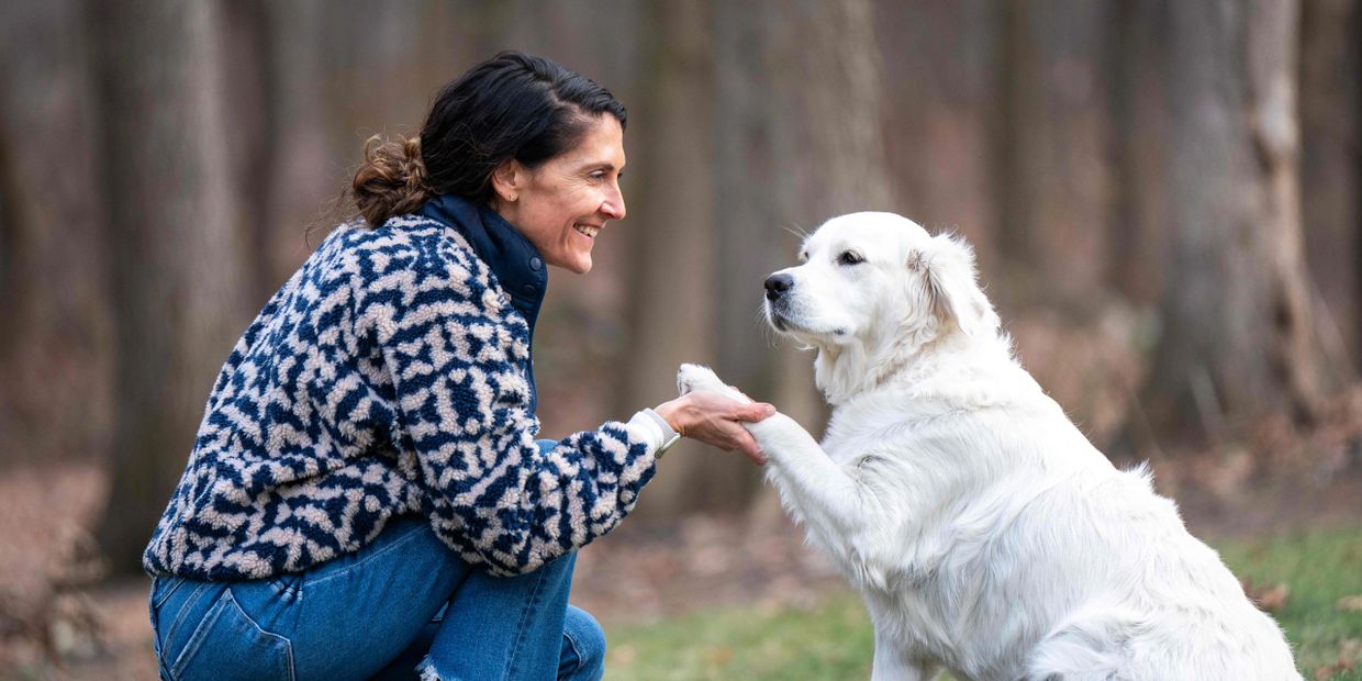 Woman happily shakes paw with a white dog outdoors.