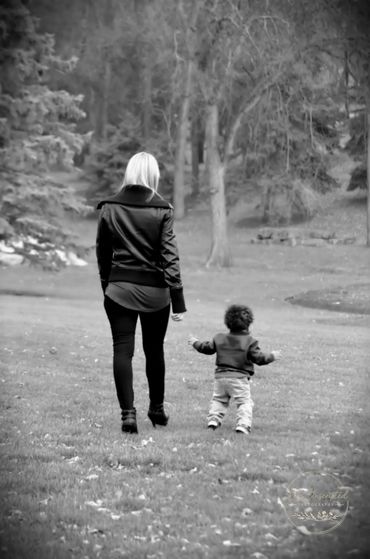 A woman and a toddler walk hand in hand through a park.