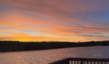 Serene sunset over a calm lake with a wooden deck in the foreground.