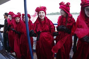 Group of people dressed in red velvet costumes with face paint on a boat.