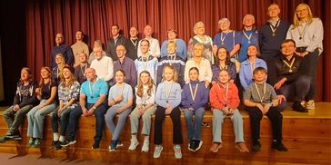 Group photo of people wearing medals on stage.