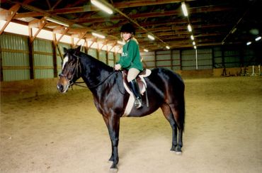 Girl wearing a green top in a riding area sitting on top of a black horse. 