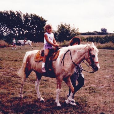 Young girl riding a pony in the 1980's being led by a woman. 