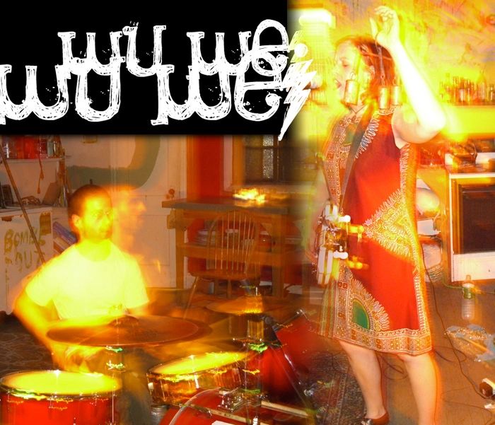 Two musicians performing in a colorful, blurred indoor setting with drums and a microphone.