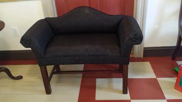 Black upholstered bench with wooden legs in a room with checkered flooring.