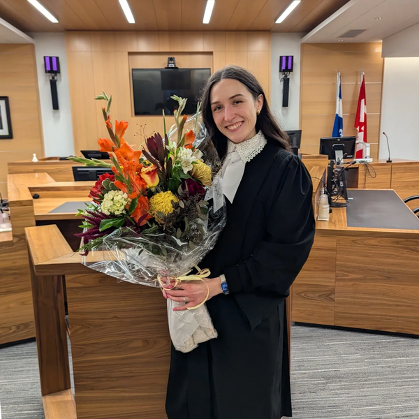 Avocate portant sa toge, son rabat et tenant un gros bouquet de fleurs pour son assermentation