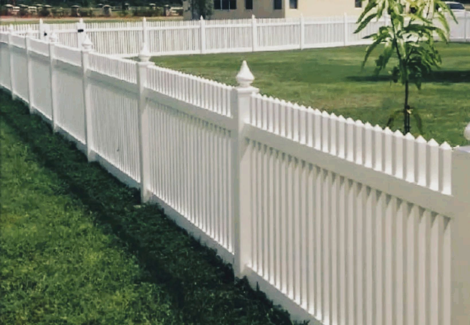Long white picket fence surrounding a green lawn.