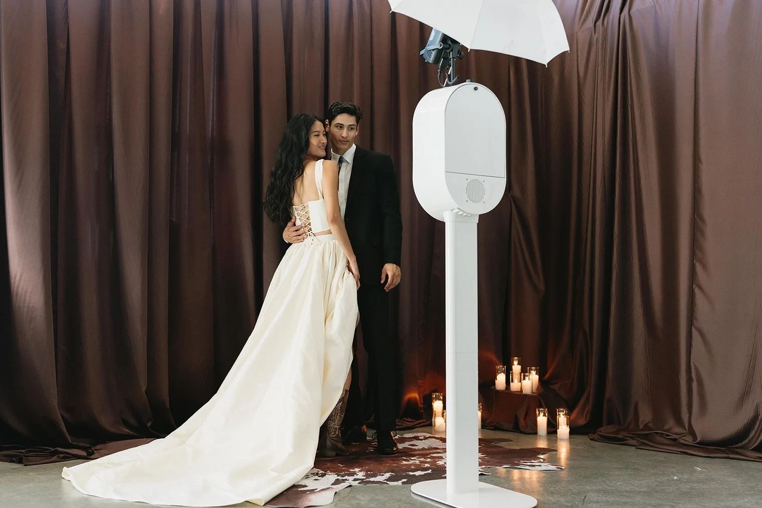 Couple posing for a photo with a photo booth and candles in the background.