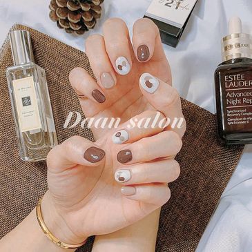Hands with stylish brown and white heart-themed nail art.