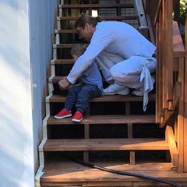 Man comforting child sitting on wooden stairs outside.