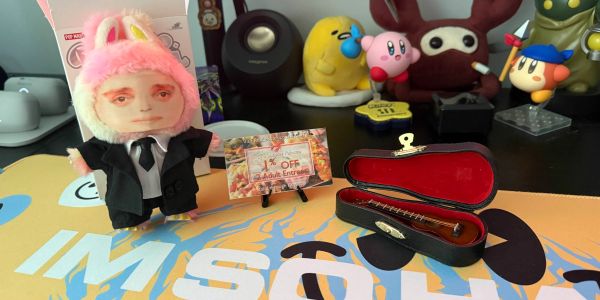 A plush doll in a suit with bunny ears next to a miniature stringed instrument in a case.