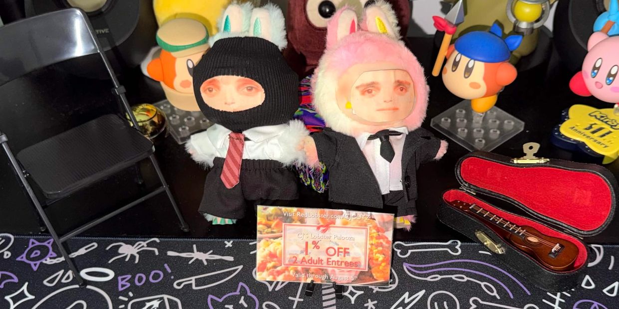 Two dolls with human faces in bunny costumes and suits hold a Red Lobster coupon on a cluttered desk.