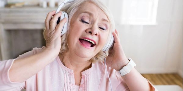 Elderly woman enjoying music with headphones, singing happily.