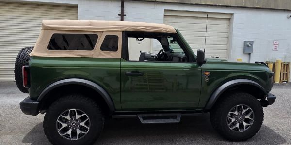 Green off-road SUV with beige soft top parked outside.