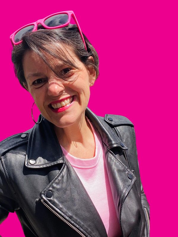 Smiling woman in black leather jacket with pink sunglasses and background.