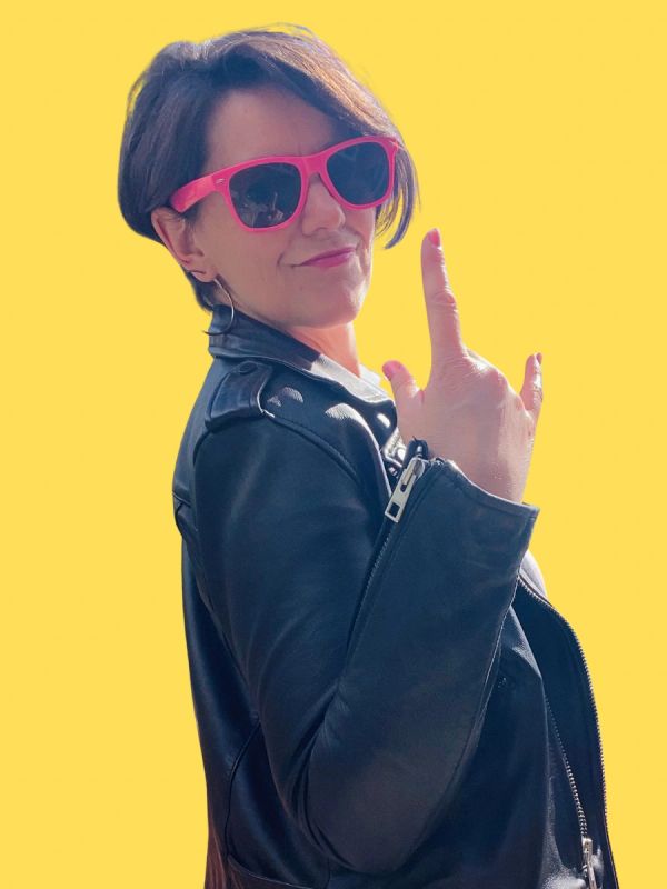 Woman in leather jacket and pink sunglasses making a rock hand gesture.