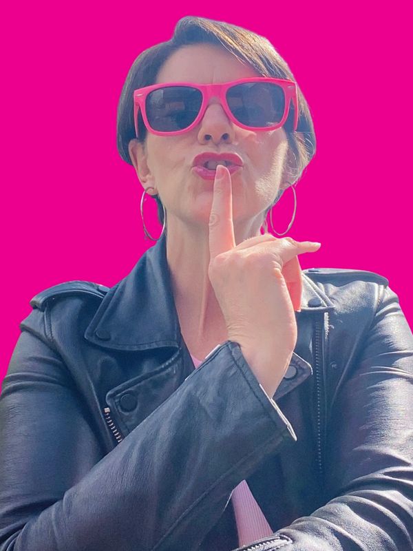 Woman in pink sunglasses and leather jacket with finger to lips.