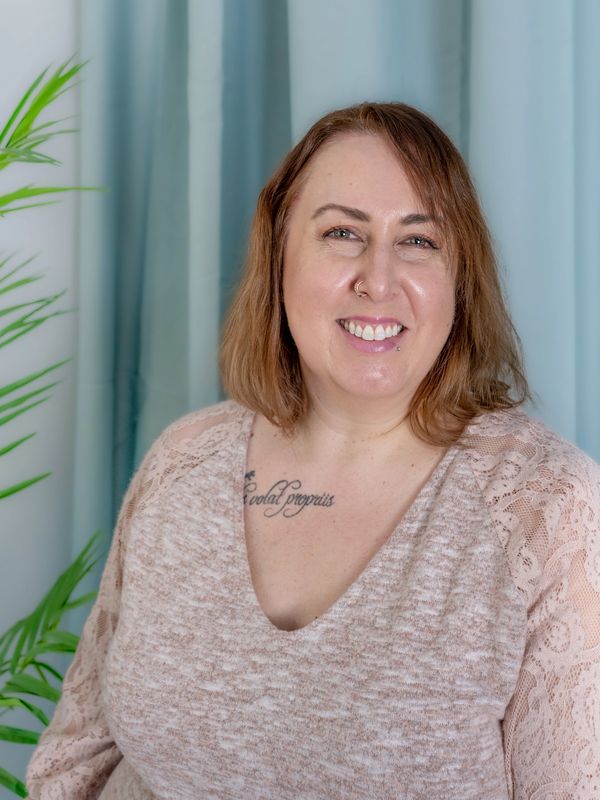 Smiling woman with tattoo and nose ring in cozy lace top.