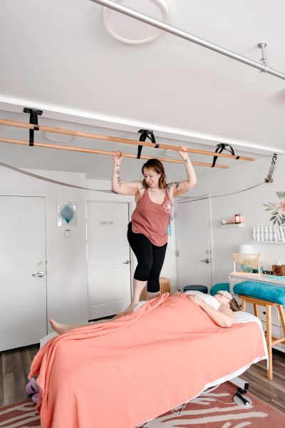 A woman balancing on a massage table above another person.