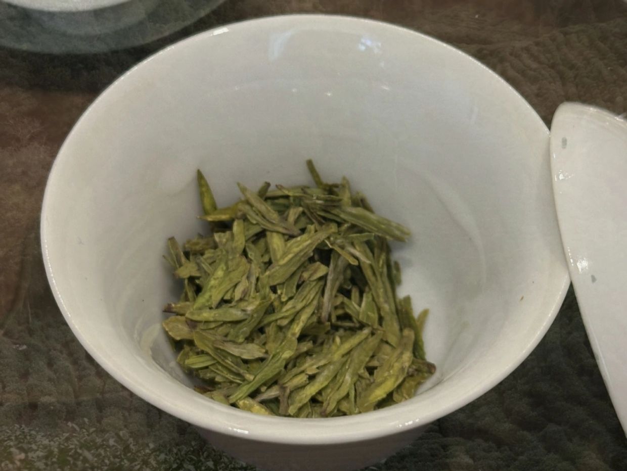 Green tea leaves in a white ceramic cup.