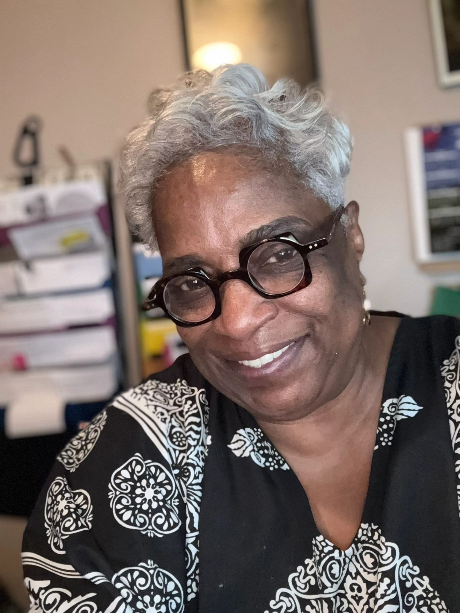 Smiling woman with gray hair and glasses.