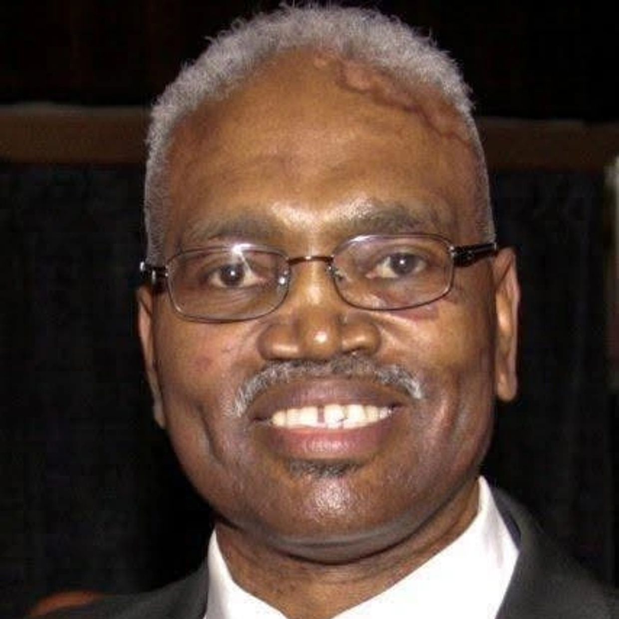Smiling elderly man with glasses and gray hair.