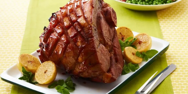 Spiral ham on platter with serving utensils and vegetables.