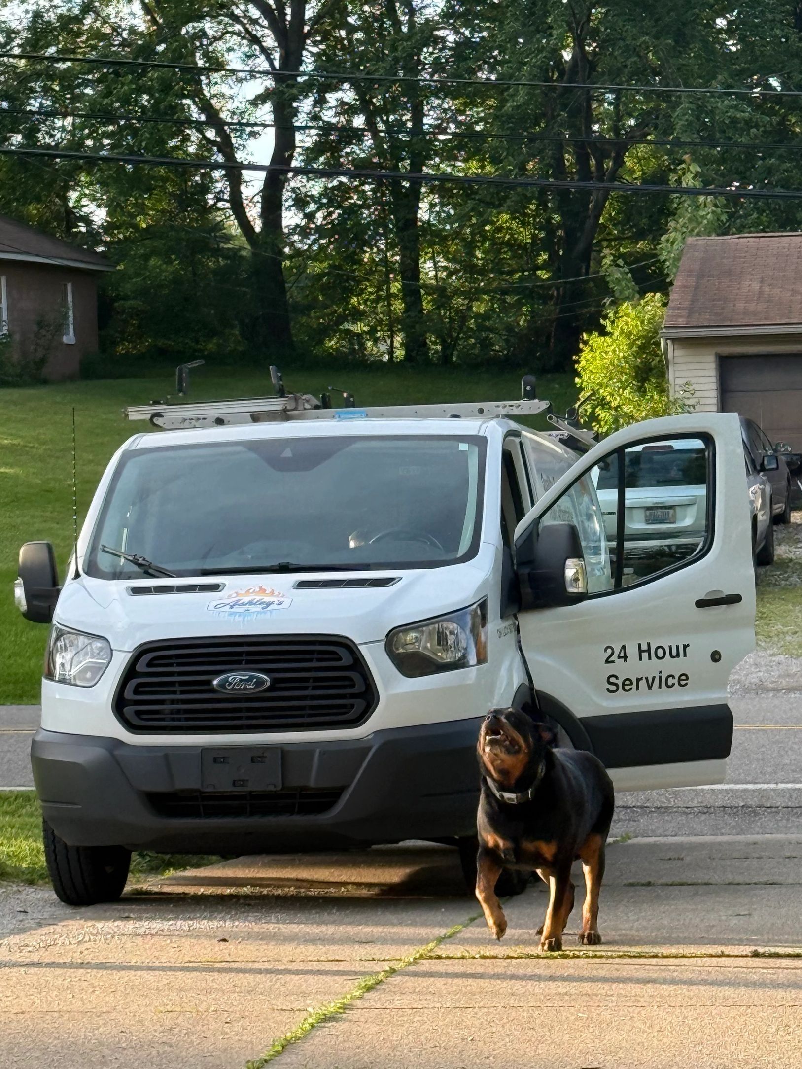 A white service van with its door open and a barking Rottweiler in front.