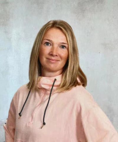 Woman with blonde hair wearing a light pink hoodie against a neutral background.
