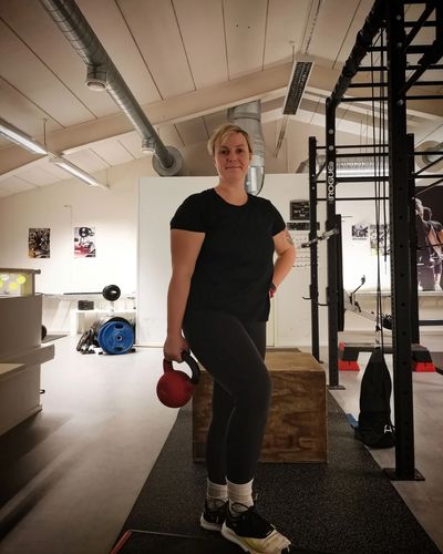 Woman in black workout clothes holding a red kettlebell in a gym.