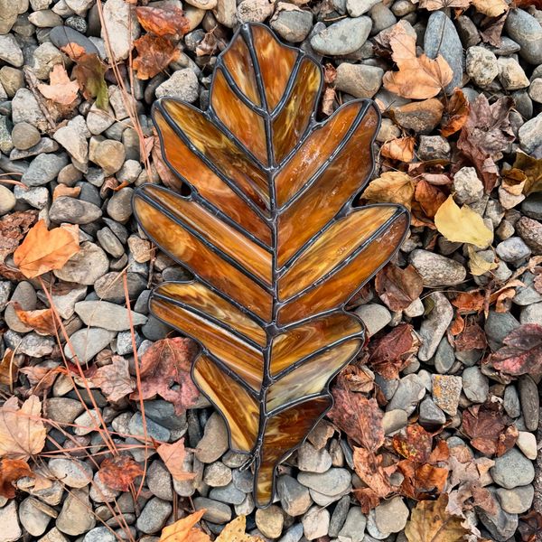 Stained glas brown oak leaf surrounded by pebbles and fall leaves. 