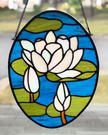 white lotus in iridescent glass, green lily pads, and dark blue water stained glass in an oval shape