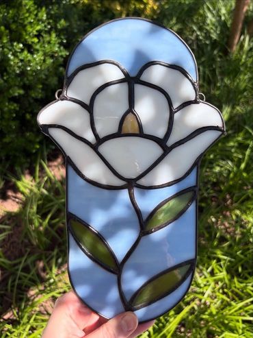 White flower with yellow stamen, green leaves, in a baby blue oval background