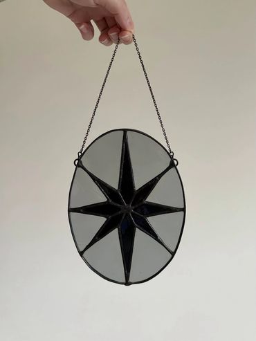 Stained glass black 8 pointed star with a grey oval background.