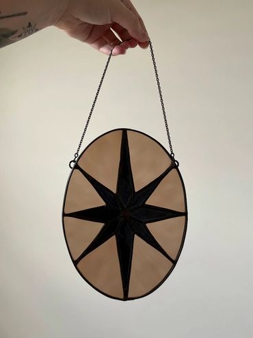 Stained glass black 8 pointed star with an amber beige oval background.