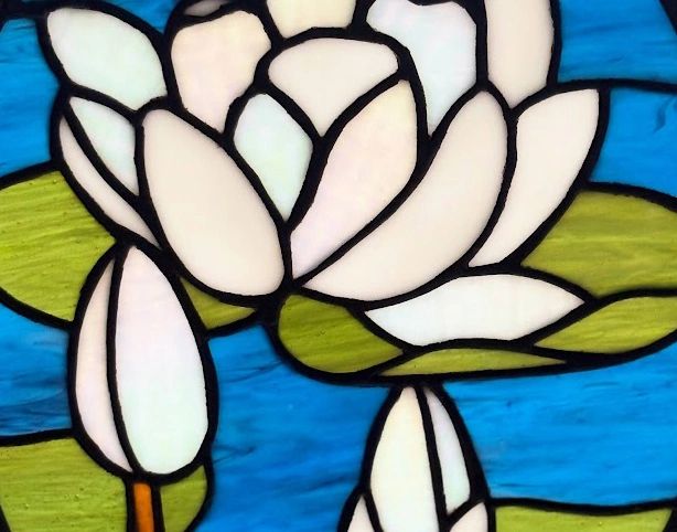 zoomed in shot of the stained glass piece of a white lotus with green lily pads and blue/black water
