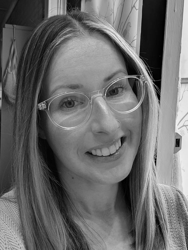 Smiling woman with glasses and long hair in a cozy indoor setting.