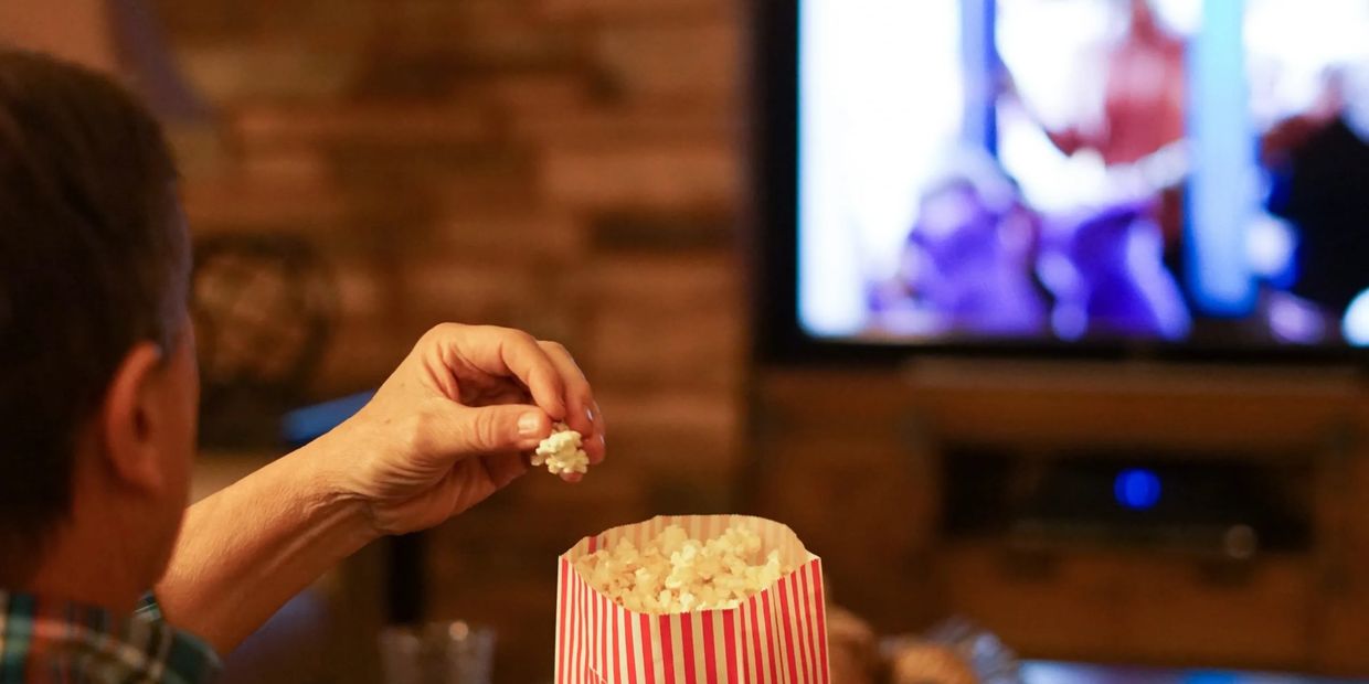 Homem comendo pipoca e assistindo televisão